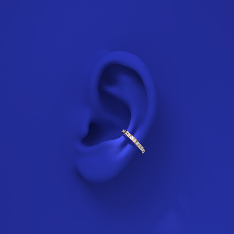 Gold earring worn on a blue ear with a matching blue background
